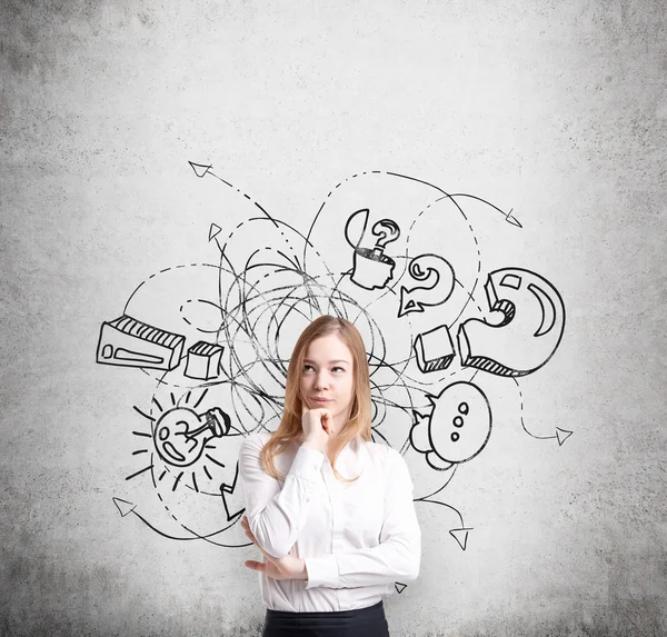 Pondering beautiful lady is trying to proceed business idea. A sketch from business icons, exclamation and question marks are drawn on the concrete wall. The concept of brainstorm process. — Stock fotografie