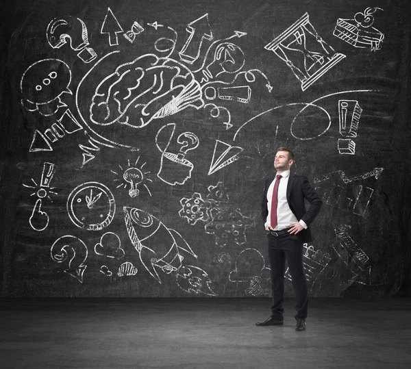 Ein selbstbewusster Geschäftsmann im formellen Anzug denkt über die Geschäftsentwicklung nach. ein skizzierter Brainstorming-Prozess wird auf die riesige schwarze Tafel gezeichnet. — Stockfoto