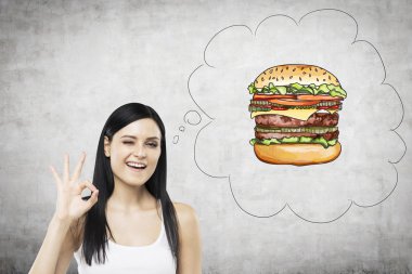 A brunette woman is thinking about burger. A fast food concept. Concrete background.