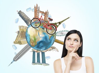 A brunette woman is dreaming about travelling. The globe with the most famous places in the world. A model of bicycle crosses of the globe. Travelling. Elements of this image furnished by NASA.