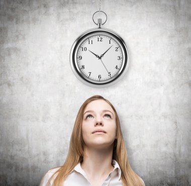 A portrait of a beautiful lady who is looking at the hovering pocket watch. A concept of a value of time in business. Concrete background.