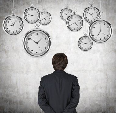A rear view of a businessman who is looking at the hovering pocket watches in the air. A concept of a value of time in business. Concrete background.