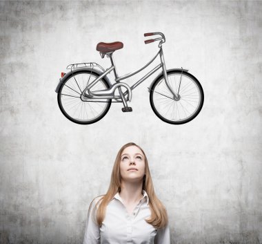A beautiful girl in formal clothes is dreaming about a new bicycle. A sketch of a bicycle is drawn on the concrete wall.