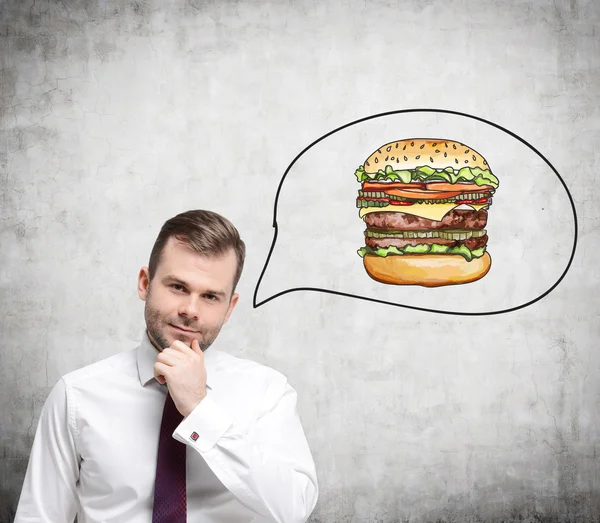 Un bel homme pense à un hamburger. Un concept de restauration rapide. Contexte concret . — Photo
