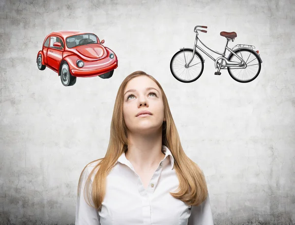 Uma mulher bonita está tentando escolher a maneira mais adequada para viajar ou viajar. Dois esboços de um carro e uma bicicleta são desenhados na parede de concreto . — Fotografia de Stock