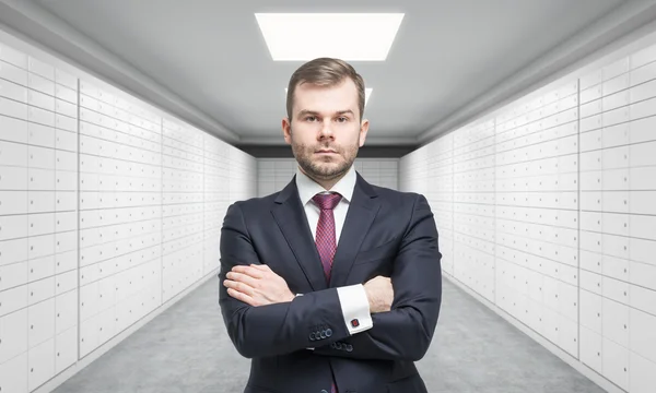 A private manger of a bank with crossed hands is standing in a room with safe deposit boxes. A concept of storing of important documents or valuables in a safe and secure environment. — Stok fotoğraf