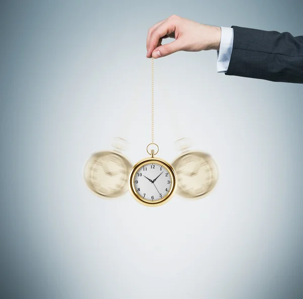 A hand holds a gold pocket watch in a chain as a pendulum. Light blue background. Time is money concept. — Stok fotoğraf