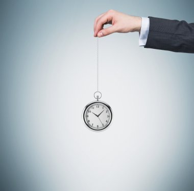 Bir el bir cep saati bir zincir içinde tutar. Açık mavi renkli. Para kavramı Zamanı.