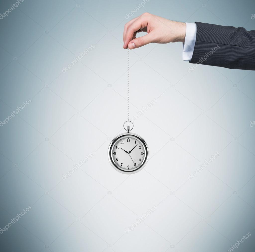 A hand holds a pocket watch in a chain. Light blue background. Time is money concept.