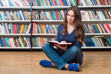 smiling young girl  sitting on the floor in the library reading 