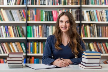 smiling young girl sitting at a desk in the library with an open