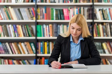 young girl with blonde hair  sitting at a desk in the library wi