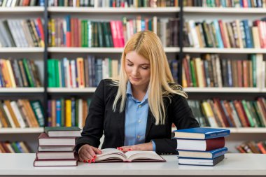 blonde young girl sitting at a desk in the library with piles of