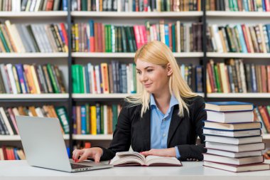 smiling young girl sitting at a desk in the library working with