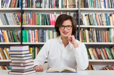 smiling young man sitting at a desk in the library with hand to 