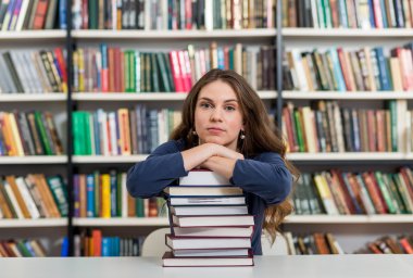 young girl sitting at a desk in the library with her arms on a b