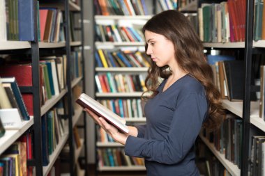 young lady standing between book shelves in the library reading 