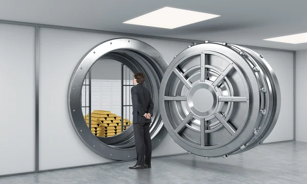 Young man standing in front of a big unlocked round metal safe i — Stockfoto