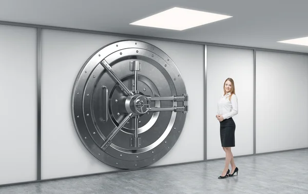 Працівник жіночого банку стоїть перед великим замкненим круглим металом — стокове фото