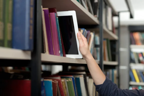 Una tableta recogida con una mano de un estante de libros en la biblioteca, un — Foto de Stock