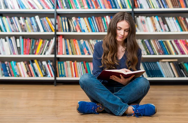 Sonriente joven sentada en el suelo en la biblioteca con cros — Foto de Stock