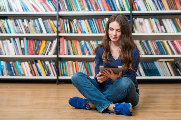 Souriant jeune fille assise sur le sol dans la bibliothèque avec des cros — Photo