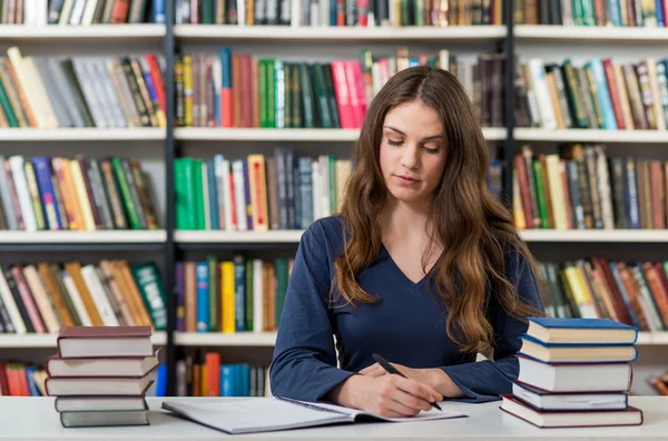 Serious young girl sitting at a desk in the library with an open — Stock fotografie