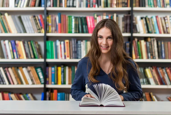 Sorridente giovane ragazza con i capelli lunghi scuri sciolti seduta a una scrivania — Foto Stock