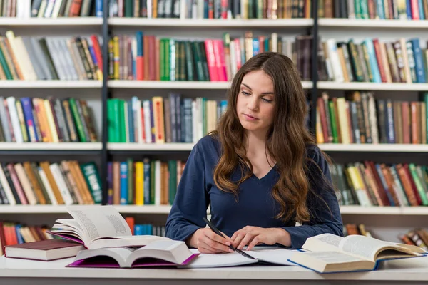 Una joven morena que está sentada en un escritorio en la biblioteca wi — Foto de Stock