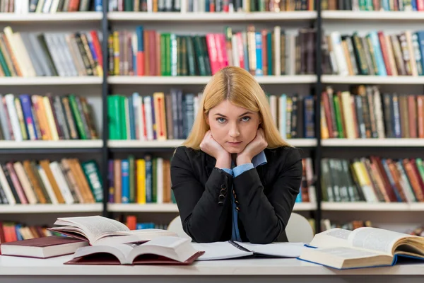 Smiling young girl with blonde hair sitting at a desk in the lib — Φωτογραφία Αρχείου