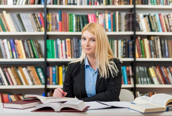 Sonriente joven con el pelo rubio sentado en un escritorio en la lib — Foto de Stock