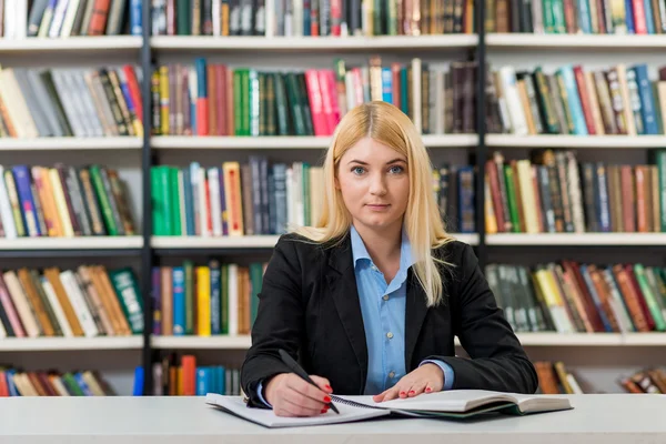 Young girl with loose blonde hair  sitting at a desk in the libr — Stockfoto