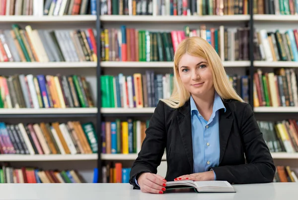 Lächelndes junges Mädchen mit blonden Haaren sitzt an einem Schreibtisch im — Stockfoto