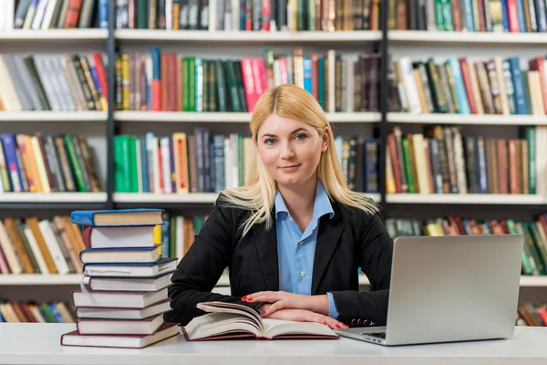 Niña sonriente sentada en un escritorio en la biblioteca trabajando con — Foto de Stock