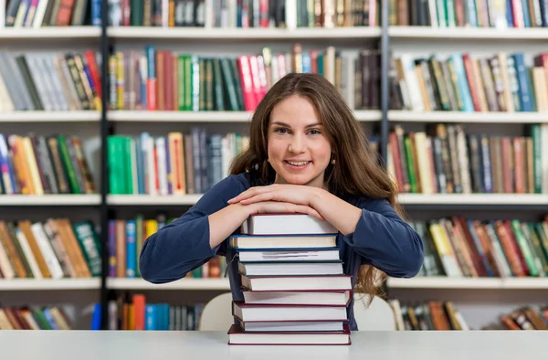 Sorrindo jovem sentada em uma mesa na biblioteca com o braço — Fotografia de Stock
