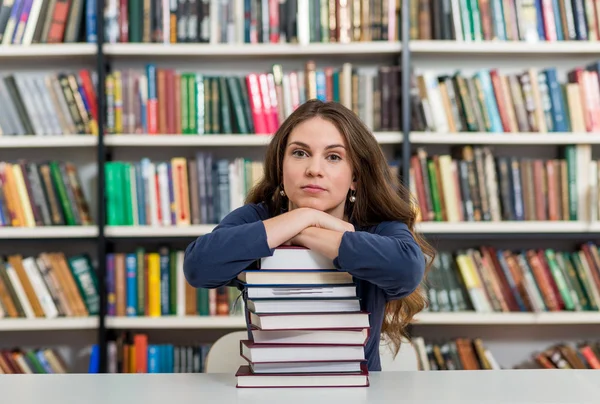 Giovane ragazza seduta ad una scrivania in biblioteca con le braccia su una b — Foto Stock