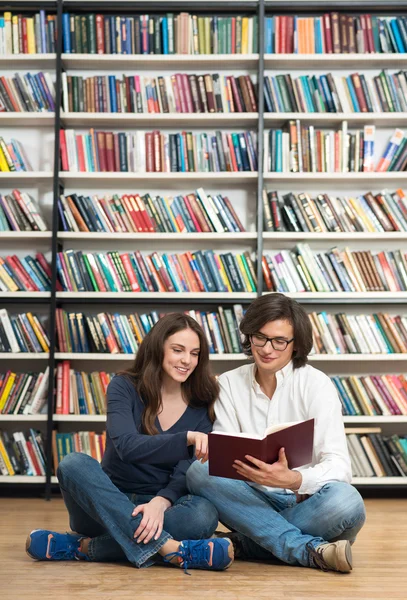 Smiling young girl and young man sitting on the floor in the lib — Stockfoto