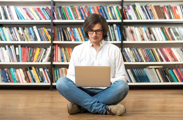 Serious young man in white shirt sitting on the floor with cross — Stockfoto