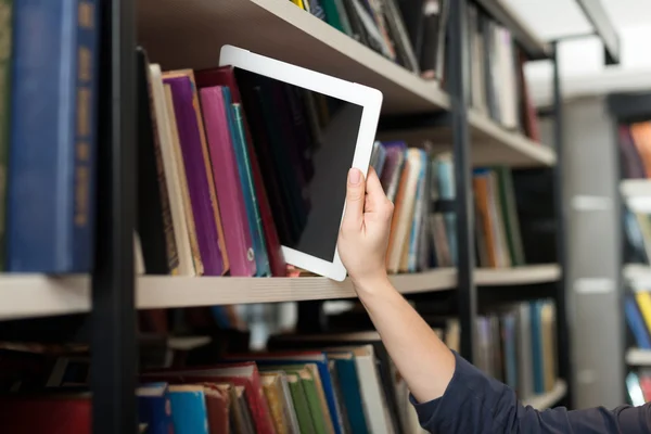 A tablet put with a hand on a book shelf in the library, a conce — Stock Photo, Image