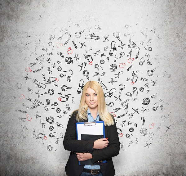 Young woman holding notebooks, wall with drawn pictures behind — Stockfoto