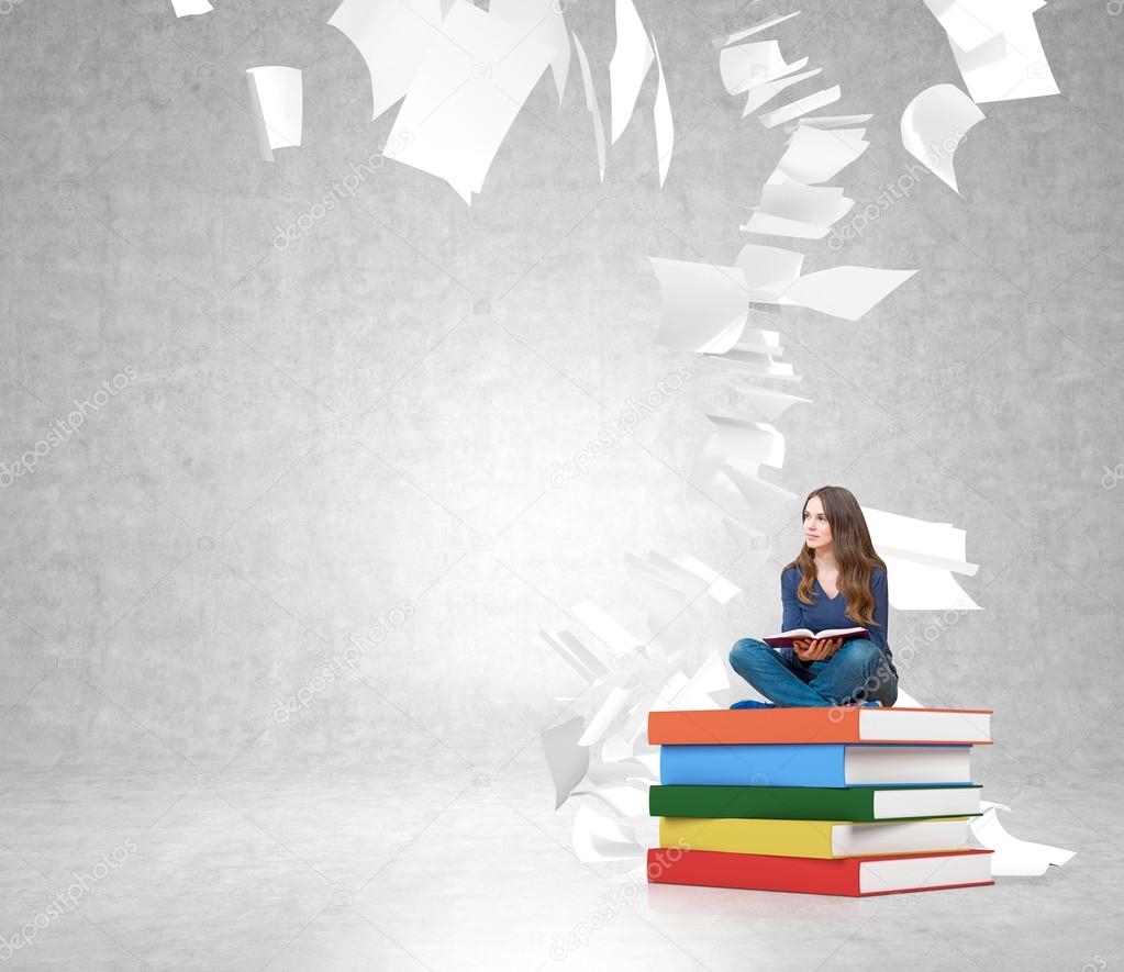 young woman on  pile of books with paper flying around