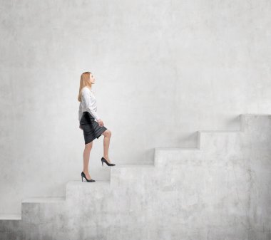 Young businesswoman going up a a concrete stairs steadily along a concrete wall.