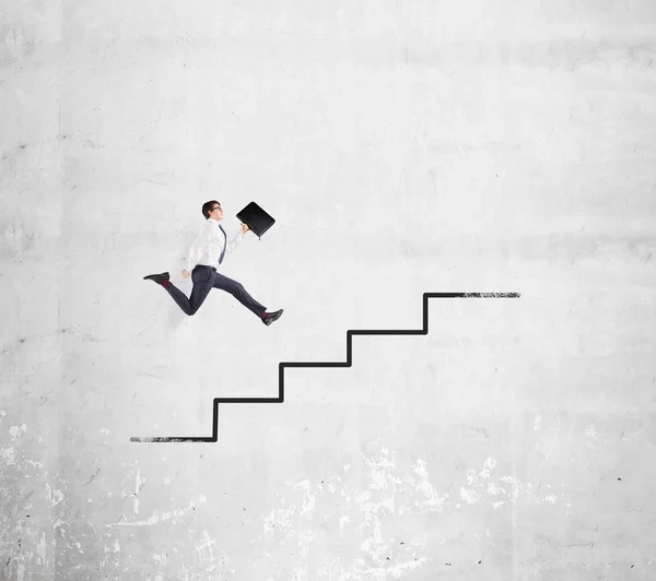 Happy young businessman with a folder running up a drawn stairs along a concrete wall. Concept of career growth. — Stock Photo, Image