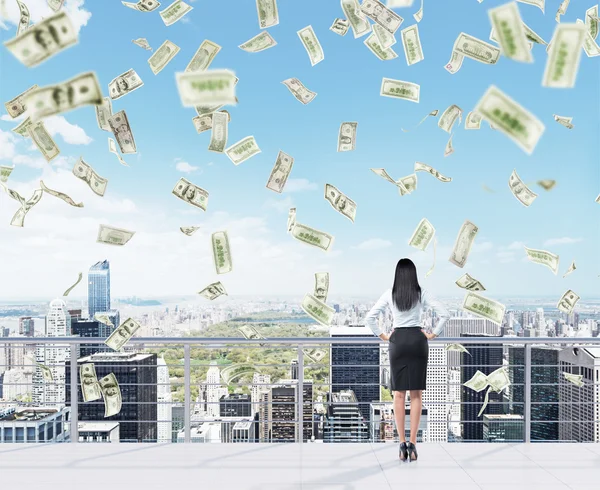 Young businesswoman with hands on hips standing on the roof of a business centre and looking at New York. Money falling from above. — Stockfoto