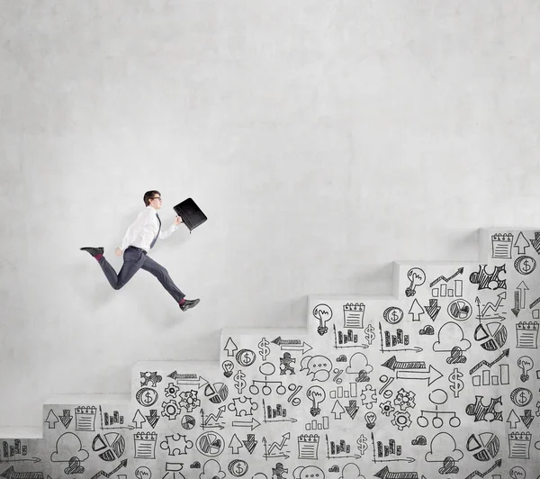 Young businessman with a folder running fast up a a concrete stairs with drawn business icons on it along a concrete wall. — Stock Fotó