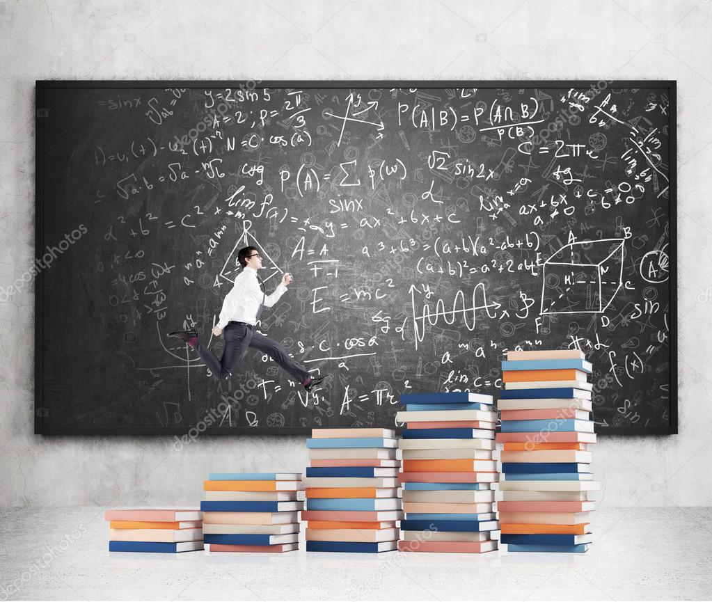 Young man with a folder in hand running up stairs made of piles of books of different size, blackboard with notes at the concrete background.