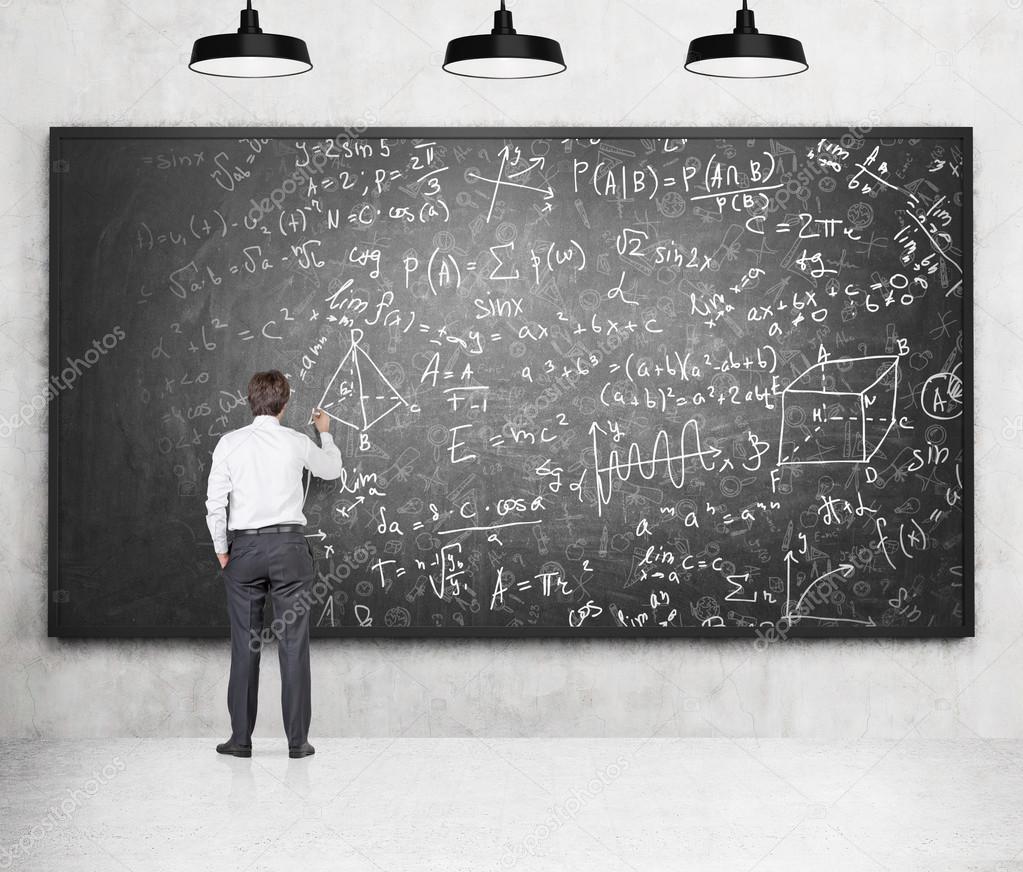 Young man writing and drawing mathimatic formulas and drafts on a black blackboard.