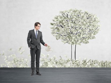 Young businessman with one hand in pocket holding a watering can pouring water on a drawn tree with dollars instead of leaves.