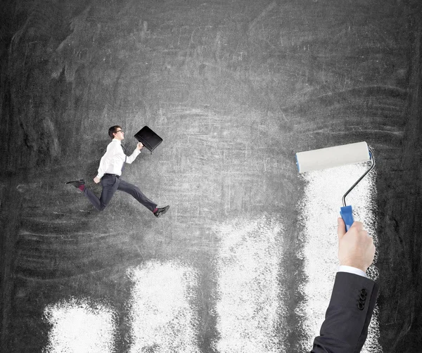 Young businessman with a folder running up a painted bar chart, hand painting the bar chart with a roler on the black background. — Stock Fotó