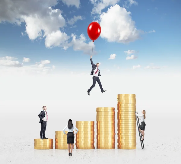 Businessman flying on a red baloon over a bar chart made of coins, another man standing on the lowest bar, woman climbing a ladder, another woman looking at them. — Stock Photo, Image